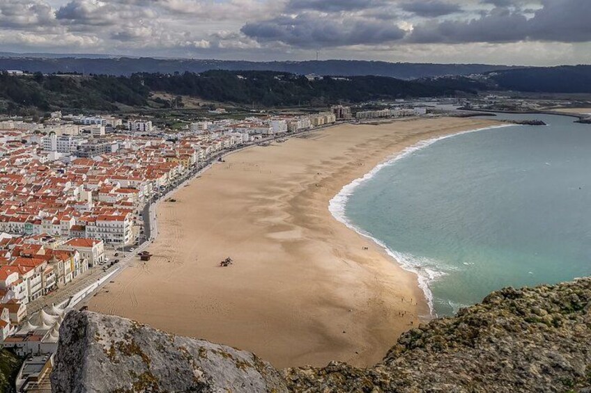 A coastal city with a long sandy beach, a clear blue sea, and a hilly landscape in the background. 4