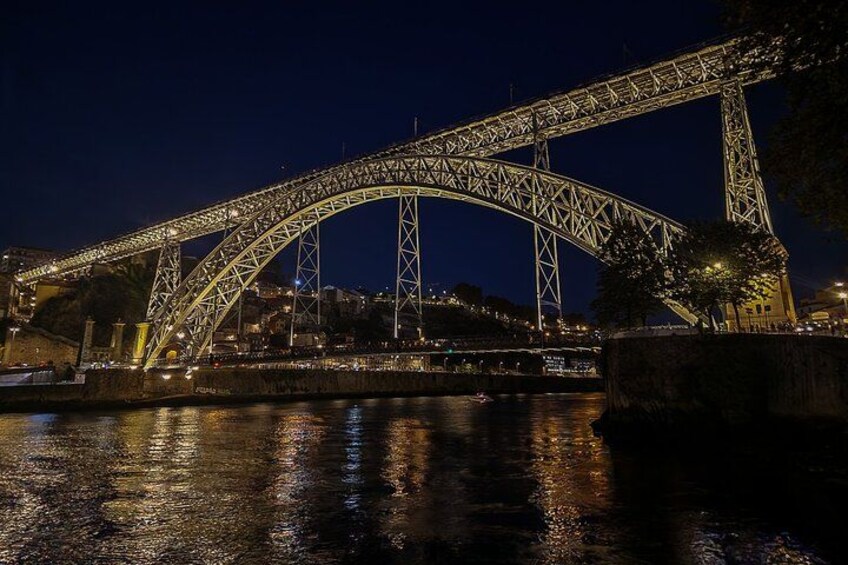 A nighttime view of a large steel bridge with its lights reflecting on the water. 5