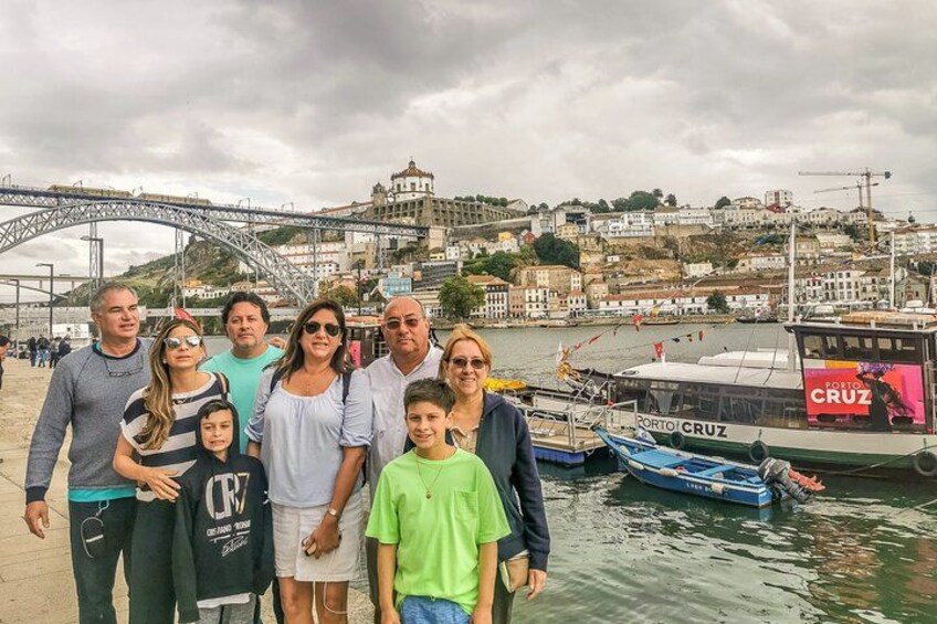 A group of people standing by a waterfront with a bridge and a boat named 'PORTO CRUZ' in the background. 3