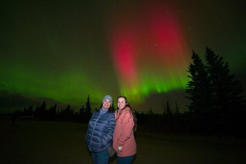 Two people standing in a field with the aurora borealis in the background. 1