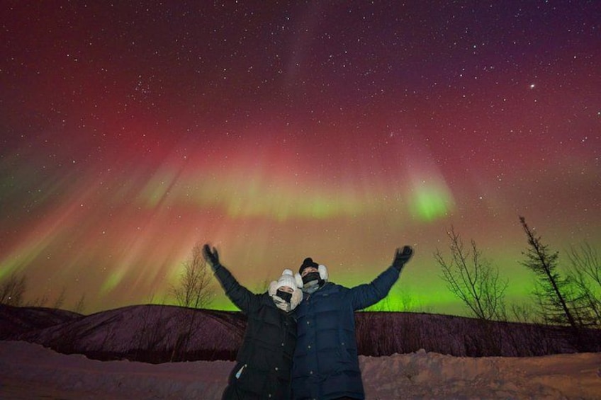 A person standing with arms raised, facing a night sky with the aurora borealis. 4