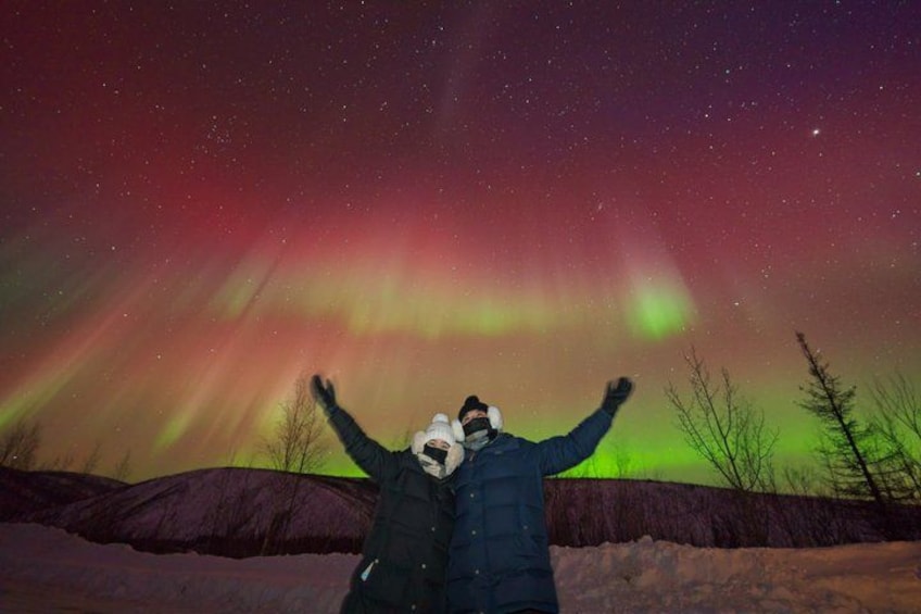 A person standing with arms raised, facing a night sky with the Northern Lights. 2
