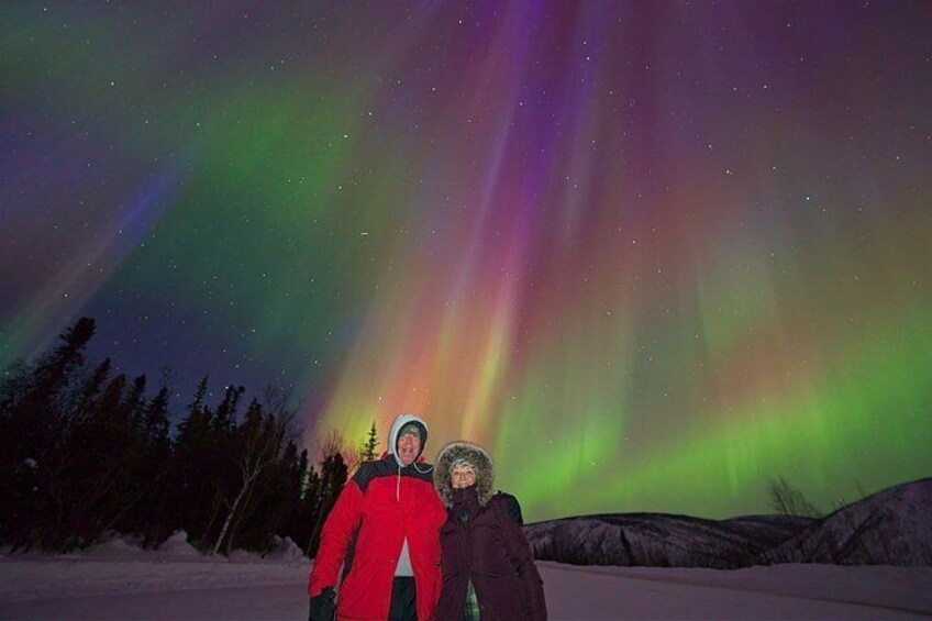 Two people standing in a snowy landscape under a vibrant aurora borealis. 1