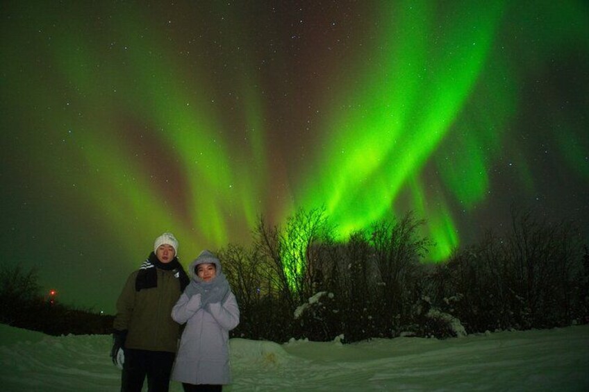 Two people standing in a snowy landscape under a night sky with green aurora borealis. 3