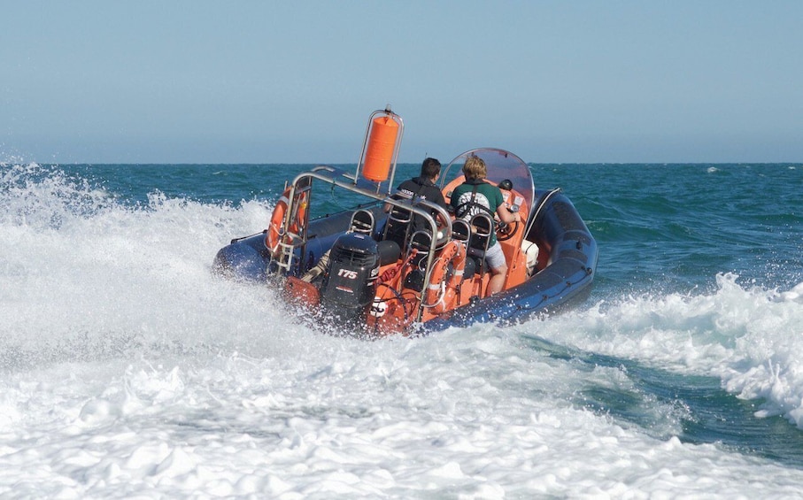 A small inflatable boat with passengers and an orange life buoy. 5