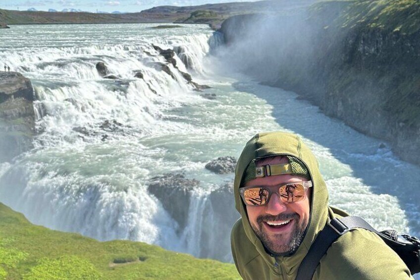 A waterfall with a person in a green jacket taking a selfie. 1