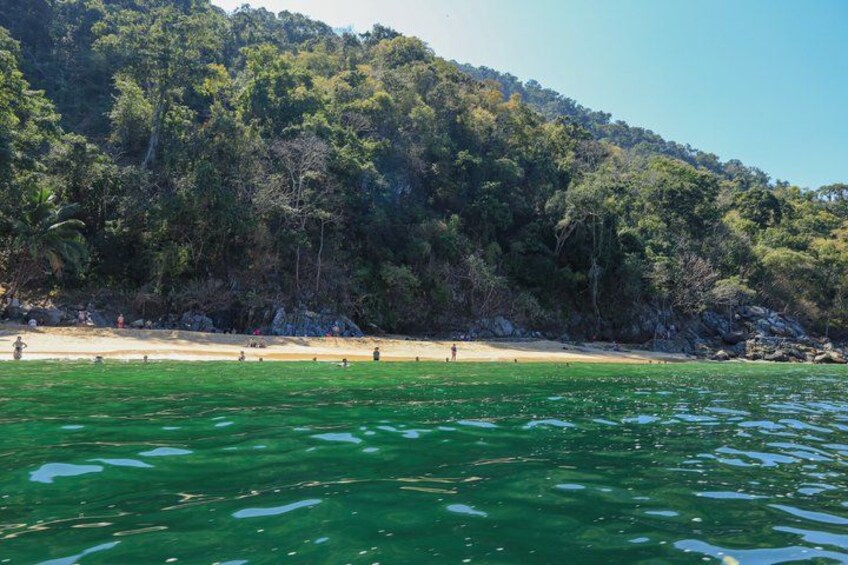 Una playa con agua cristalina, una orilla arenosa y una colina arbolada al fondo. 2