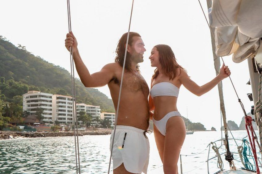 Una pareja en un velero con un paisaje urbano costero al fondo. 4