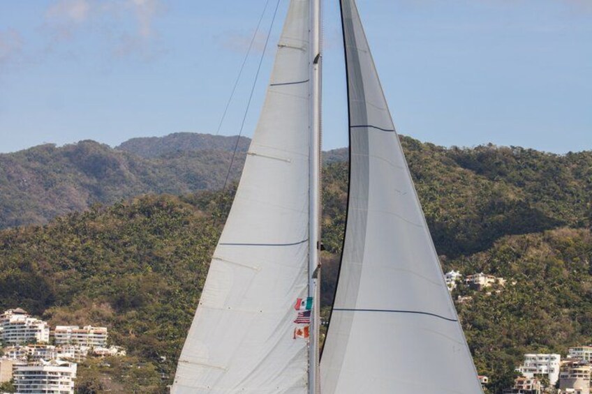 Un velero con dos velas, un paisaje montañoso y edificios al fondo. 3