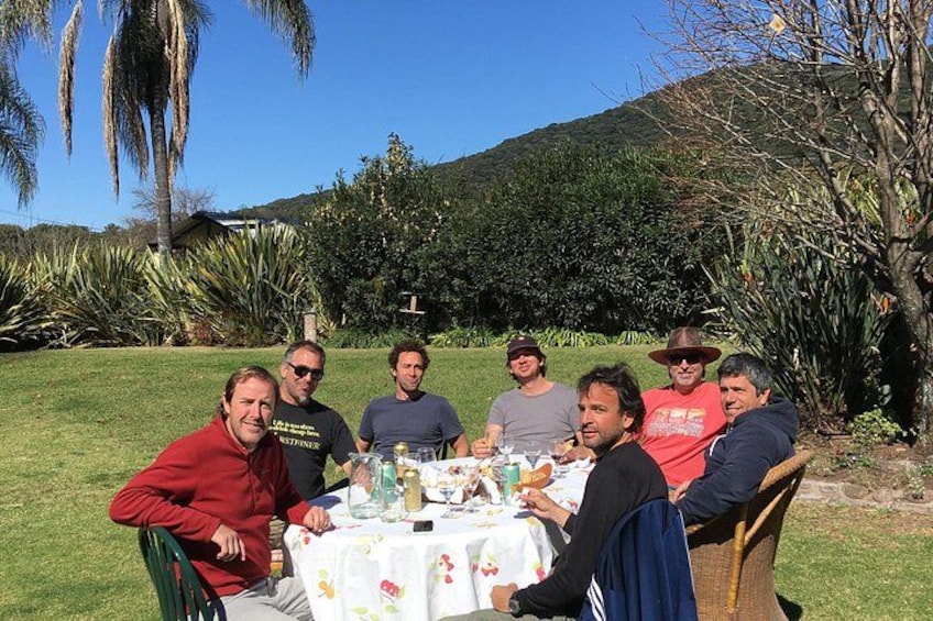 A group of people seated around a table outdoors with a grassy area and trees in the background. 2