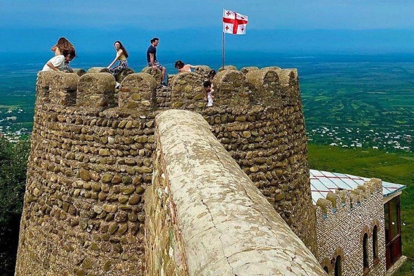 Un muro di pietra di un castello con una bandiera, che domina un paesaggio costiero. 3