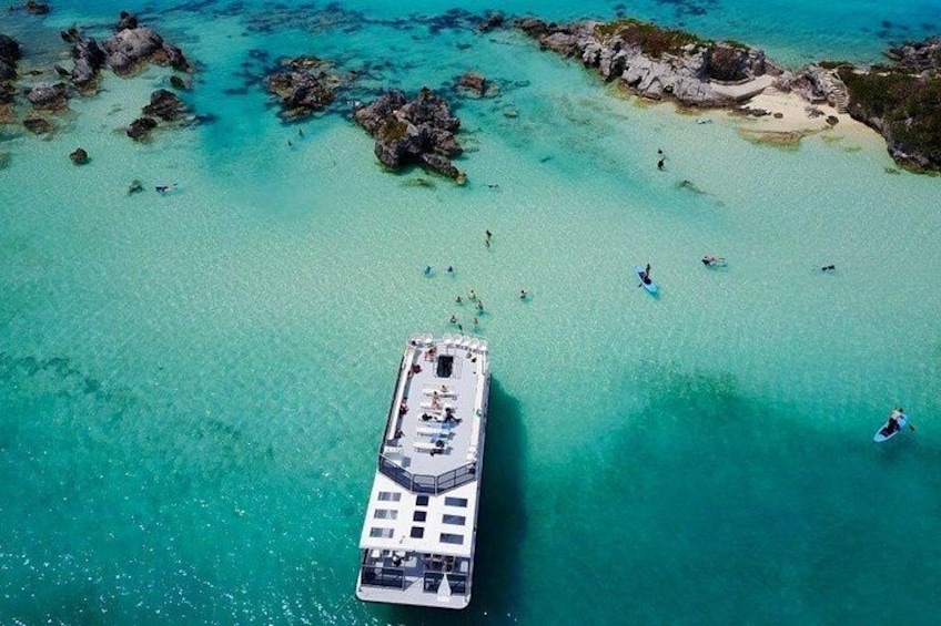 A cruise ship in turquoise waters with rocky outcrops and people swimming. 4