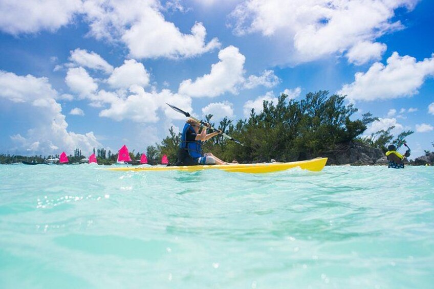 A person kayaking on turquoise water with a clear sky and palm trees in the background. 2
