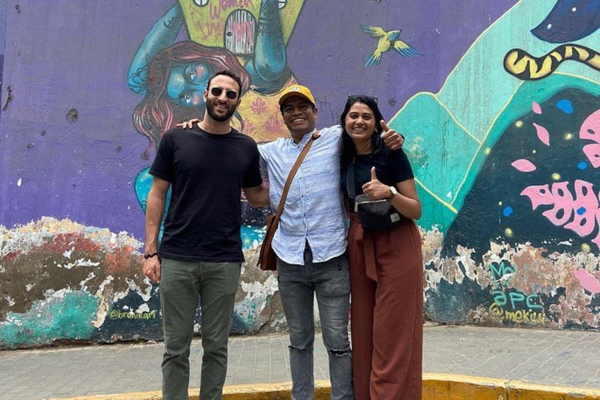 Three people standing in front of a colorful mural with abstract figures and text. 3