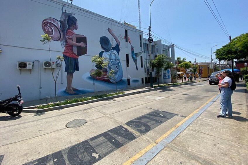 A mural on a building, a street with a sidewalk, and a person standing on the sidewalk. 5