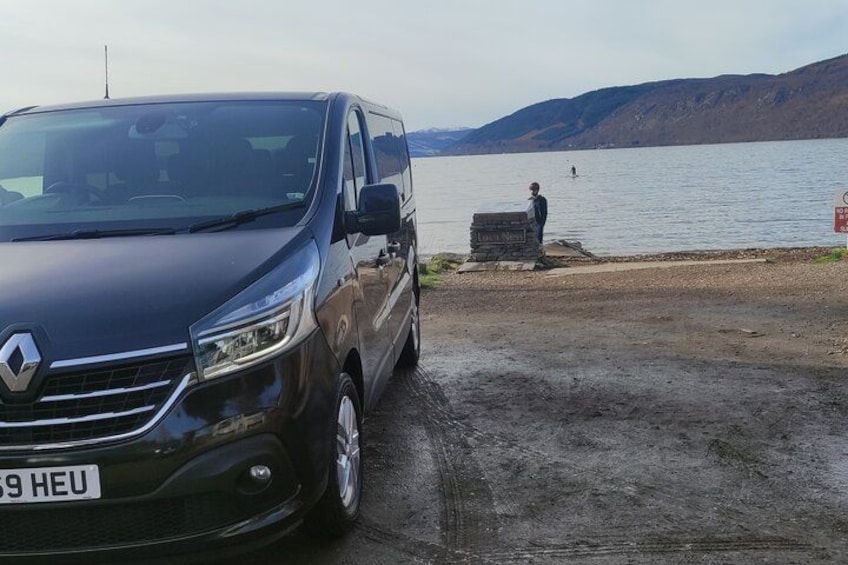 A black car parked by a lake with a person standing in the background. 5