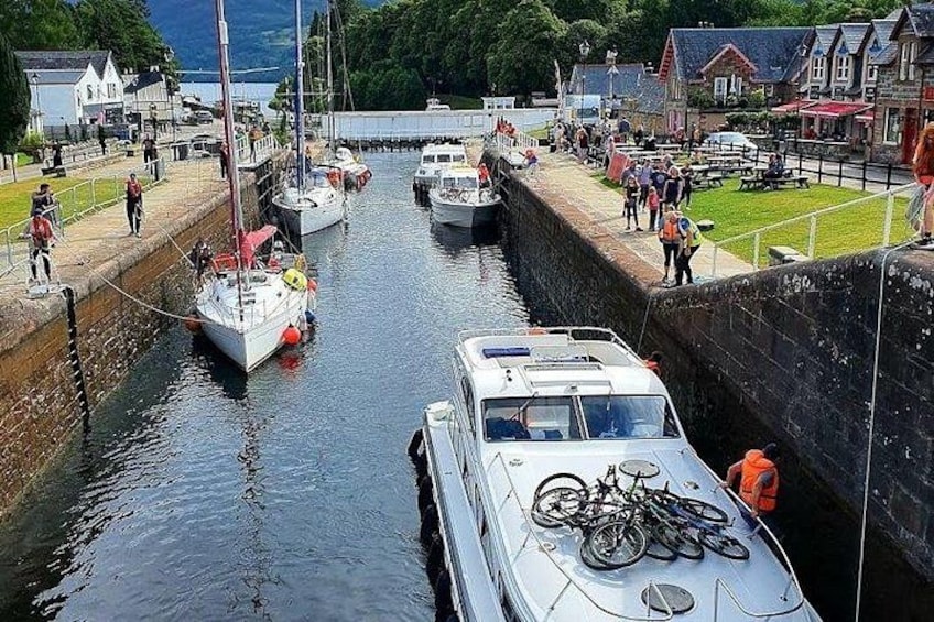 Un canal con barcos, un sistema de esclusas y un pueblo con edificios y gente. 3