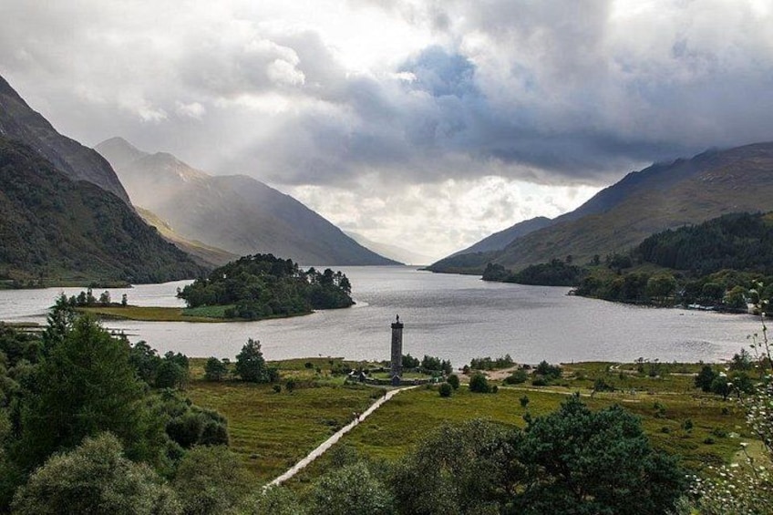 Un lago rodeado de montañas, un faro y una zona con césped y árboles. 2