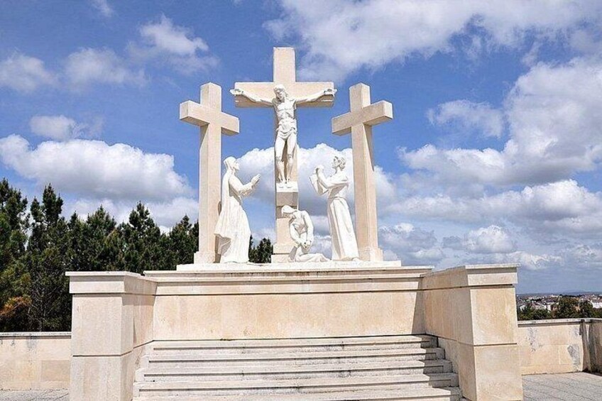 A white religious monument with a cross, figures of Jesus, and two women, set against a clear sky. 3