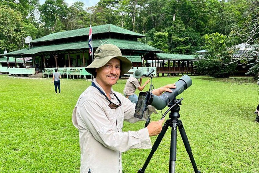 A person using a telescope on a grassy field with a green-roofed building in the background. 1