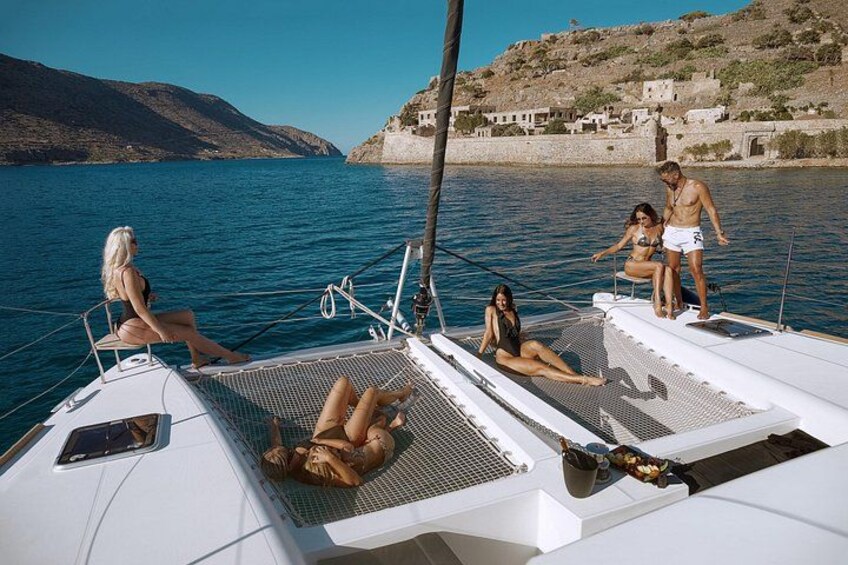Ein Segelboot mit entspannten Personen auf dem Deck, ruhiges Meer und ein Küstendorf im Hintergrund. 5