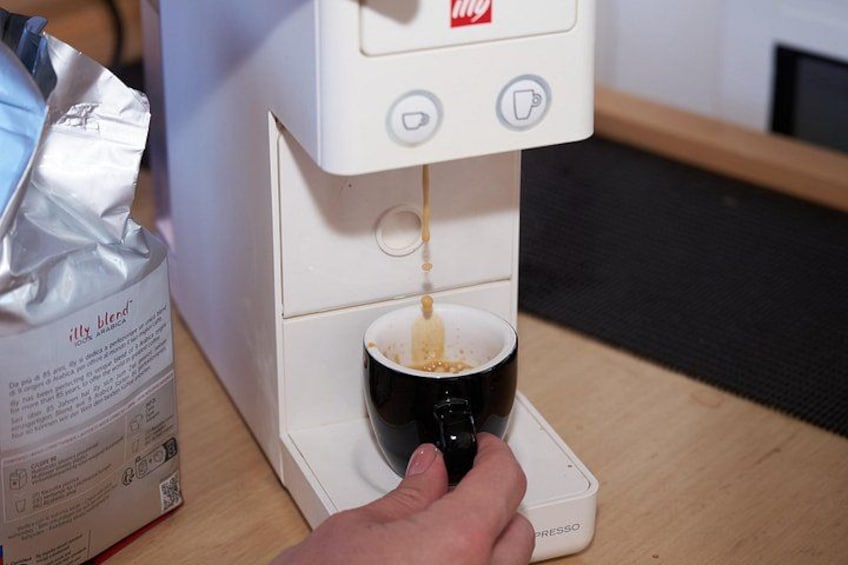 Eine Hand drückt eine Taste an einer Kaffeemaschine, die Kaffee in eine schwarze Tasse abgibt. 2