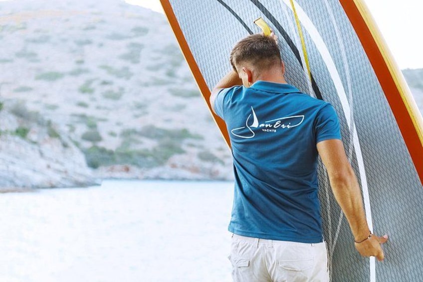 Eine Person steht neben einem Surfbrett, im Hintergrund eine gebirgige Landschaft. 3