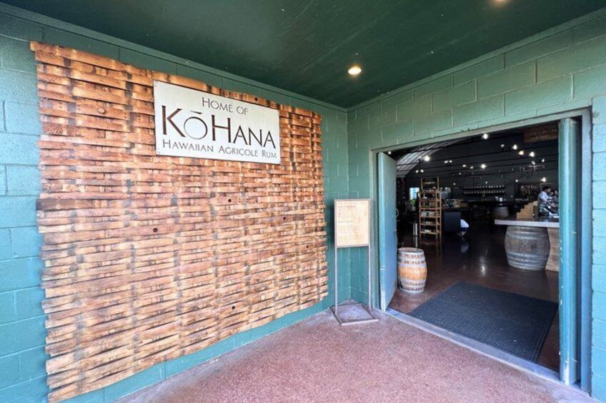 En mur av tegelstenar med en skylt som lyder: ”Här tillverkas Kohana Hawaiian Agricole Rom”, och en dörr som leder inåt. 3