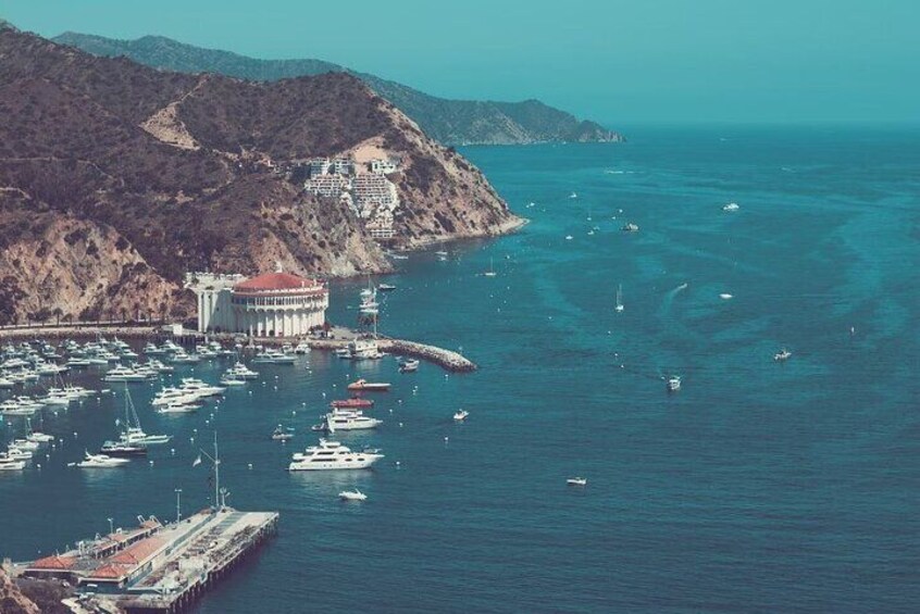 Marina costera con barcos, un edificio grande y montañas al fondo. 1