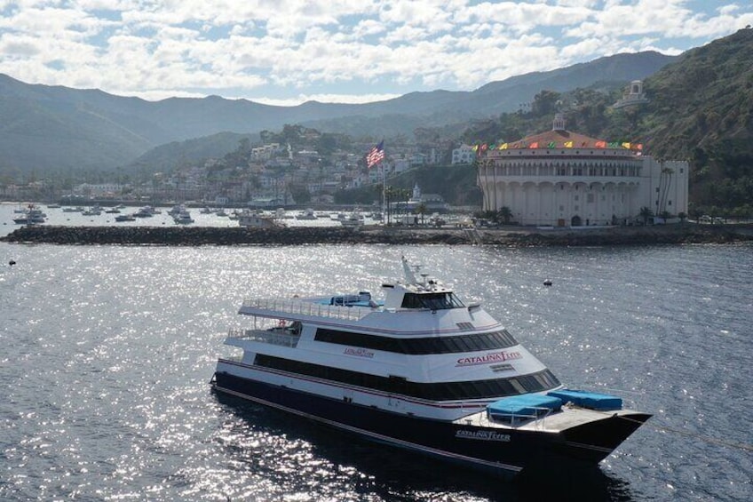 Un barco blanco y negro llamado Catalina Express sobre aguas con montañas y un edificio al fondo. 4