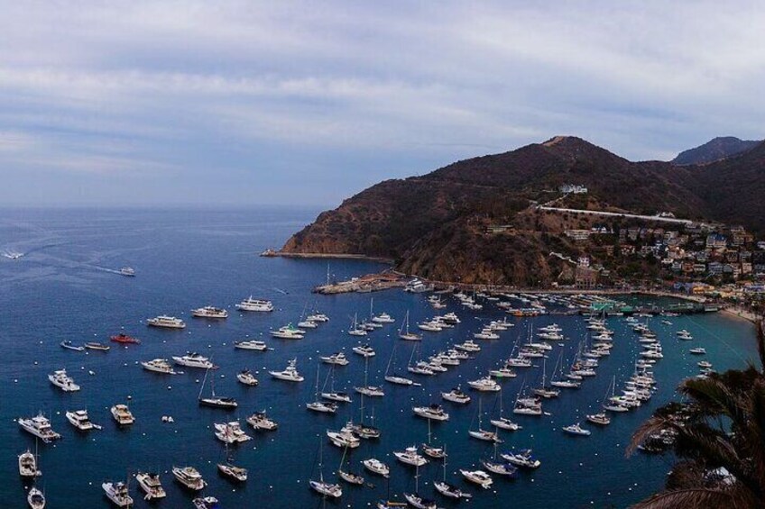 Un pueblo costero con numerosos barcos amarrados en un puerto deportivo, rodeado de colinas y un cielo despejado. 2