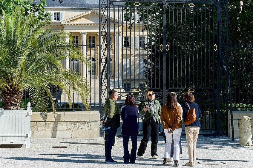 Un groupe de personnes se tient devant un portail en métal noir orné d’éléments décoratifs. 1