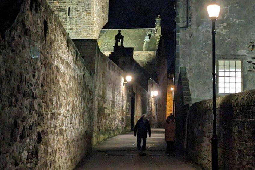A stone pathway flanked by old buildings, a person walking, and a street lamp. 2