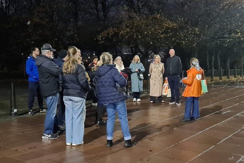 A group of people standing on a wet pavement at night, with trees in the background. 4