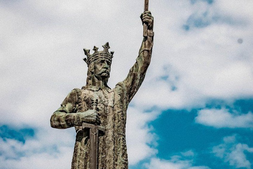 A statue of a crowned figure holding a staff, set against a cloudy sky. 1