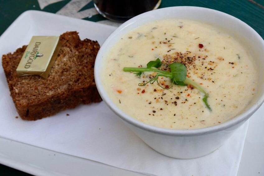 Eine Schale cremige Suppe mit Kräutern und eine Scheibe Brot mit Butter auf einem weißen Teller. 4