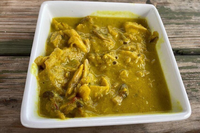 Un plato cuadrado blanco con curry amarillo, trozos de carne y especias. 3