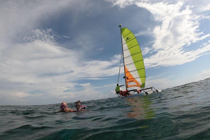 A person on a sailboard and two people swimming in the ocean. 2
