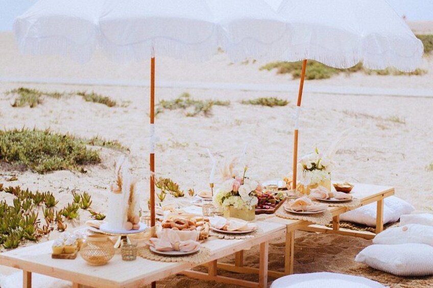 A beachside picnic setup with tables, umbrellas, and food. 1