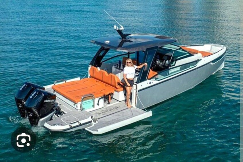 A motorboat with a cabin, an outboard motor, and a seating area with orange cushions. 1
