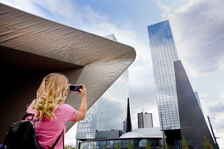 A person taking a photo of a tall, modern skyscraper with a curved roof. 3