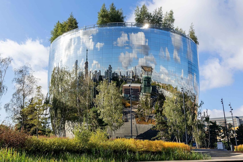 A modern glass building with a curved facade, surrounded by trees and a grassy area. 2