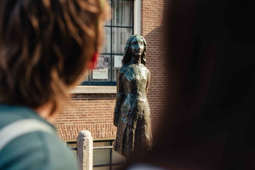 A bronze statue of a woman in a dress, with a brick building and a window in the background. 3
