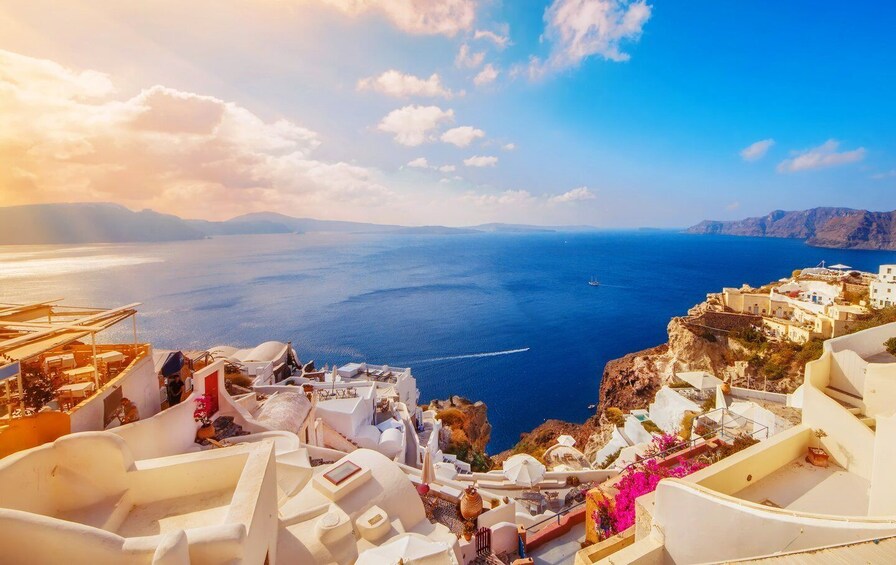A coastal town with white buildings, a clear blue sea, and a mountainous backdrop. 3