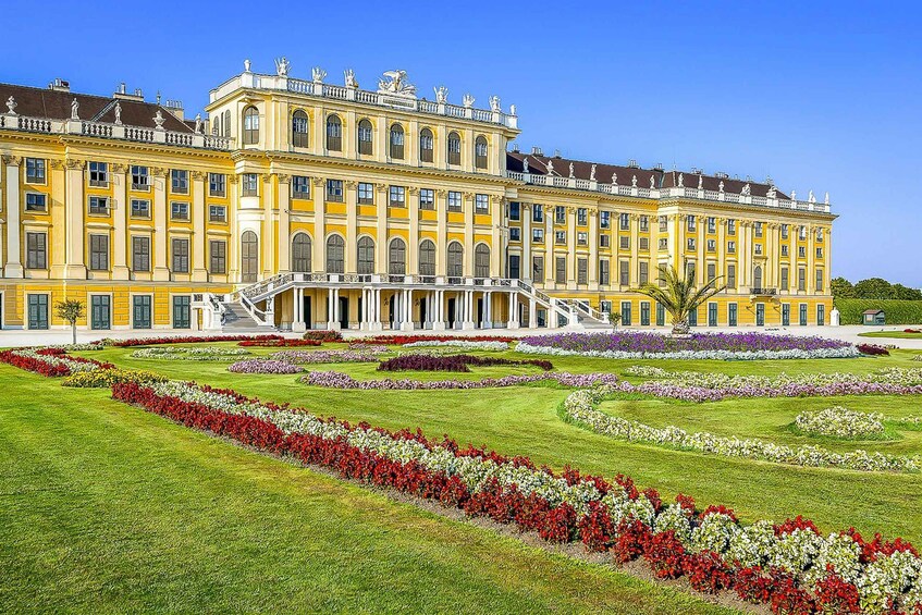 A large, yellow building with a symmetrical facade, surrounded by manicured gardens and a clear blue sky. 5