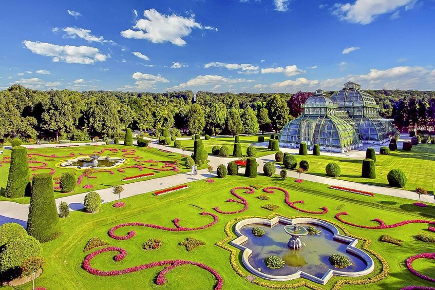 A meticulously landscaped garden with geometric flower beds, a central fountain, and a large glass conservatory. 2