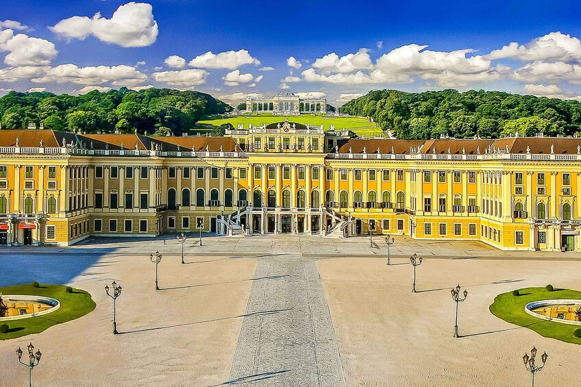 A grand palace with symmetrical architecture, a central courtyard, and a lush green hill in the background. 3