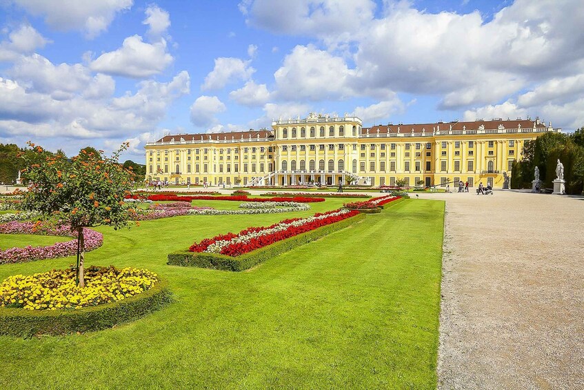 A large, classical building with symmetrical architecture, surrounded by well-manicured gardens and a clear sky. 1