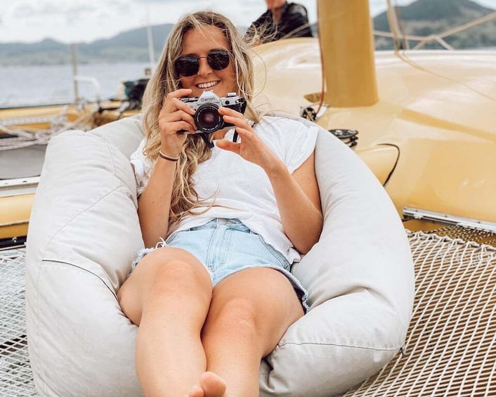 A person sitting on a white bean bag chair on a boat, holding a camera. 1