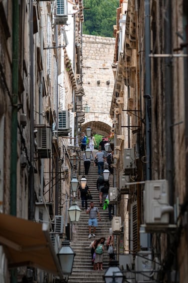 A narrow street with stone buildings, a stone bridge, and people walking up and down the stairs. 2